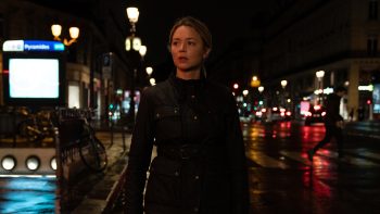 A woman walks down a street in Paris at night.